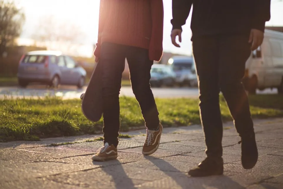 Two people walking arm in arm along a leafy park path in soft afternoon light
