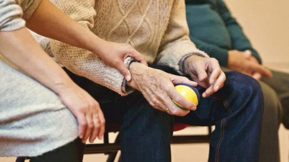 A carer's hands gently supporting an older person's hands around a mug of tea